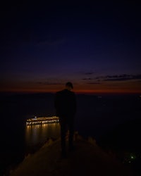 a man standing on a hill overlooking a ship at night